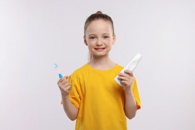 Photo of Happy girl holding toothbrush and tube of toothpaste on white background