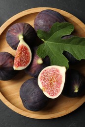 Photo of Plate with fresh ripe figs and green leaf on black table, top view