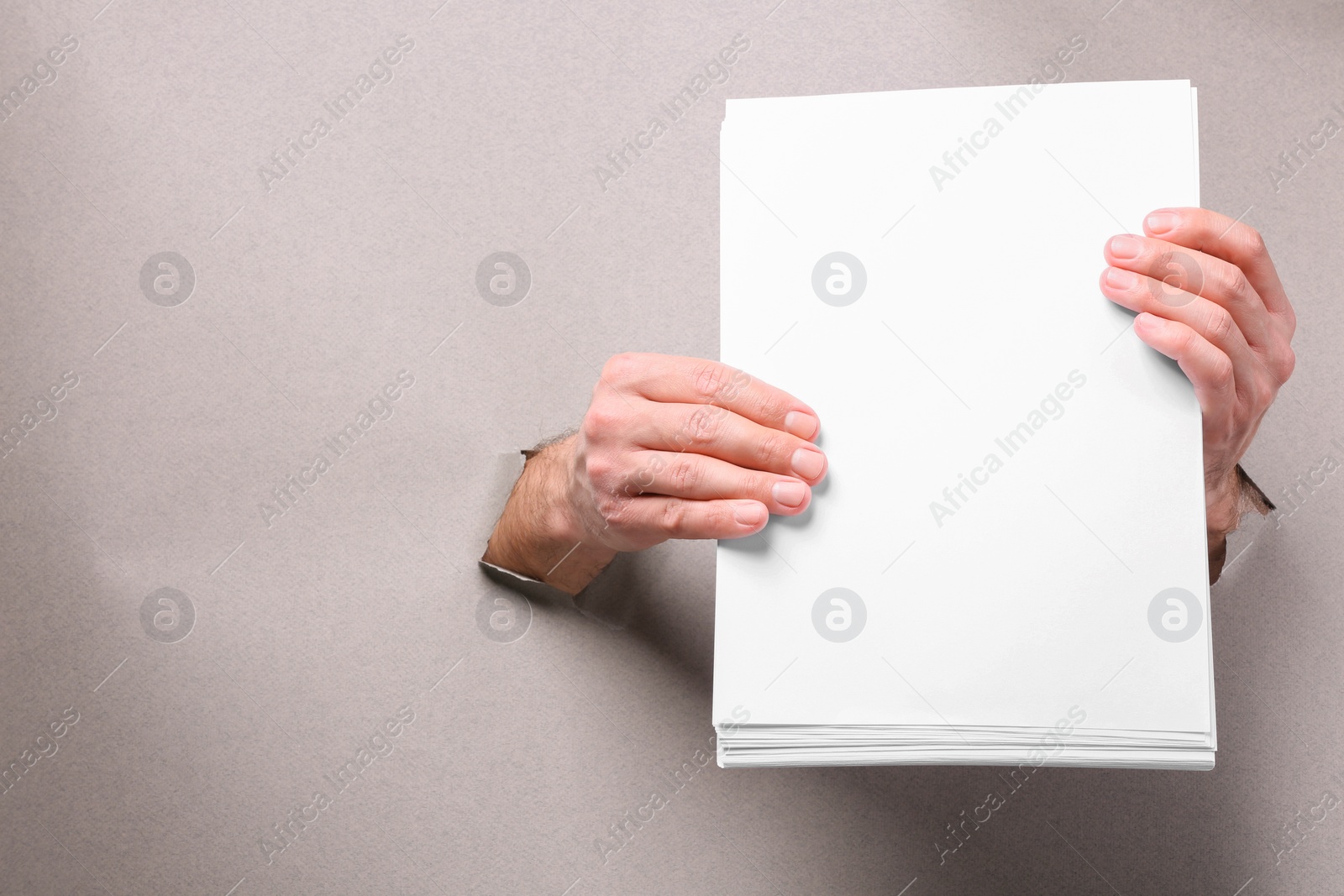 Photo of Man holding sheets of paper through holes in white paper, closeup. Mockup for design