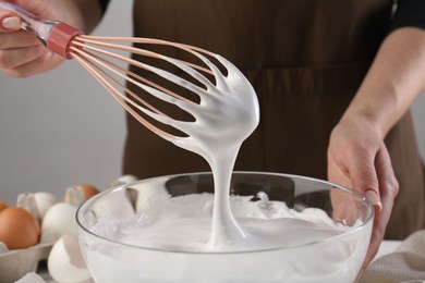 Photo of Woman making whipped cream with whisk at table, closeup