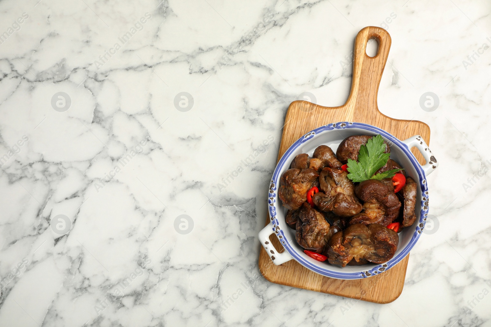 Photo of Bowl with delicious kidneys, pepper and parsley on white marble table, top view. Space for text