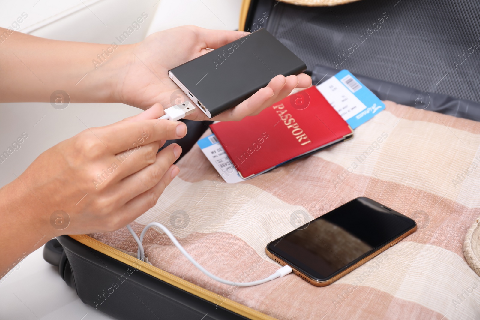 Photo of Woman charging smartphone with power bank near packed suitcase indoors, closeup