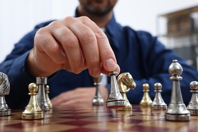Man with game piece playing chess at checkerboard indoors, closeup