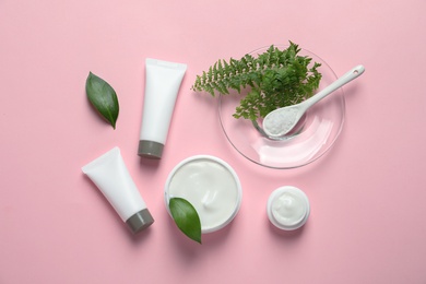 Different skin care cosmetic products with green leaves on color background, top view