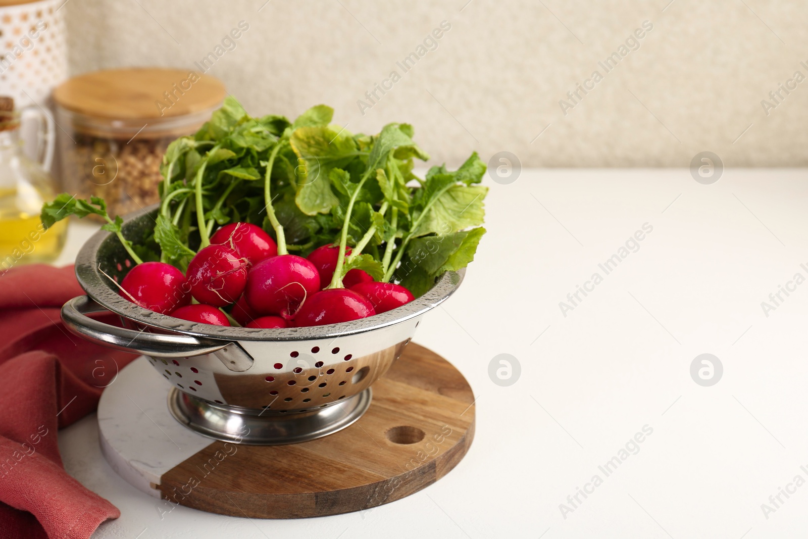 Photo of Wet radish in colander on white table, closeup. Space for text