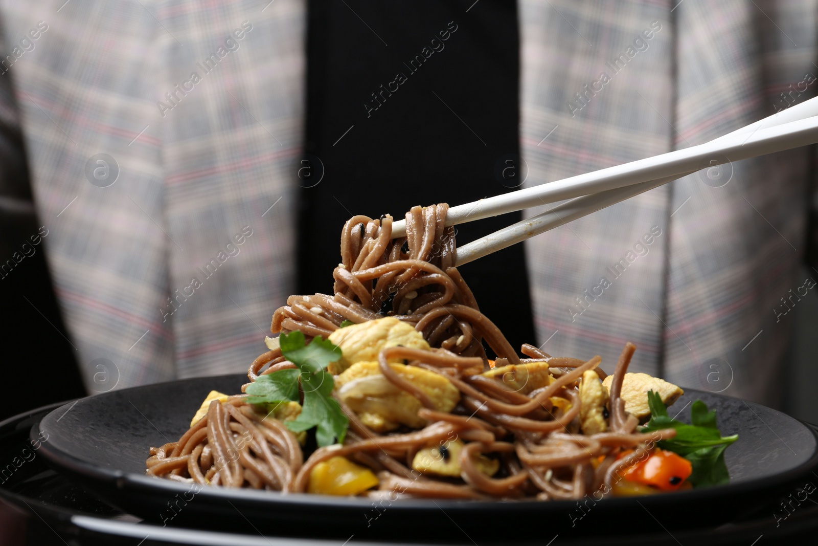 Photo of Stir-fry. Woman eating tasty noodles with meat and vegetables at table, closeup