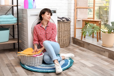 Young woman with basket full of clean clothes near washing machine at home