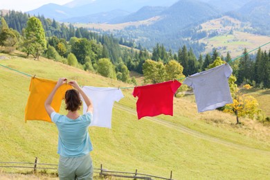 Photo of Woman hanging clean laundry with clothespins on washing line in mountains, back view