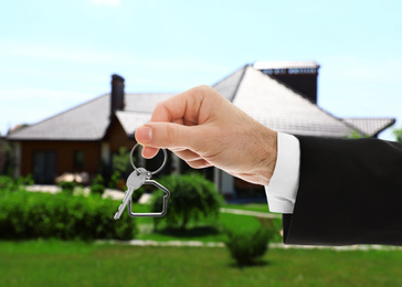 Real estate agent holding key against beautiful house, closeup