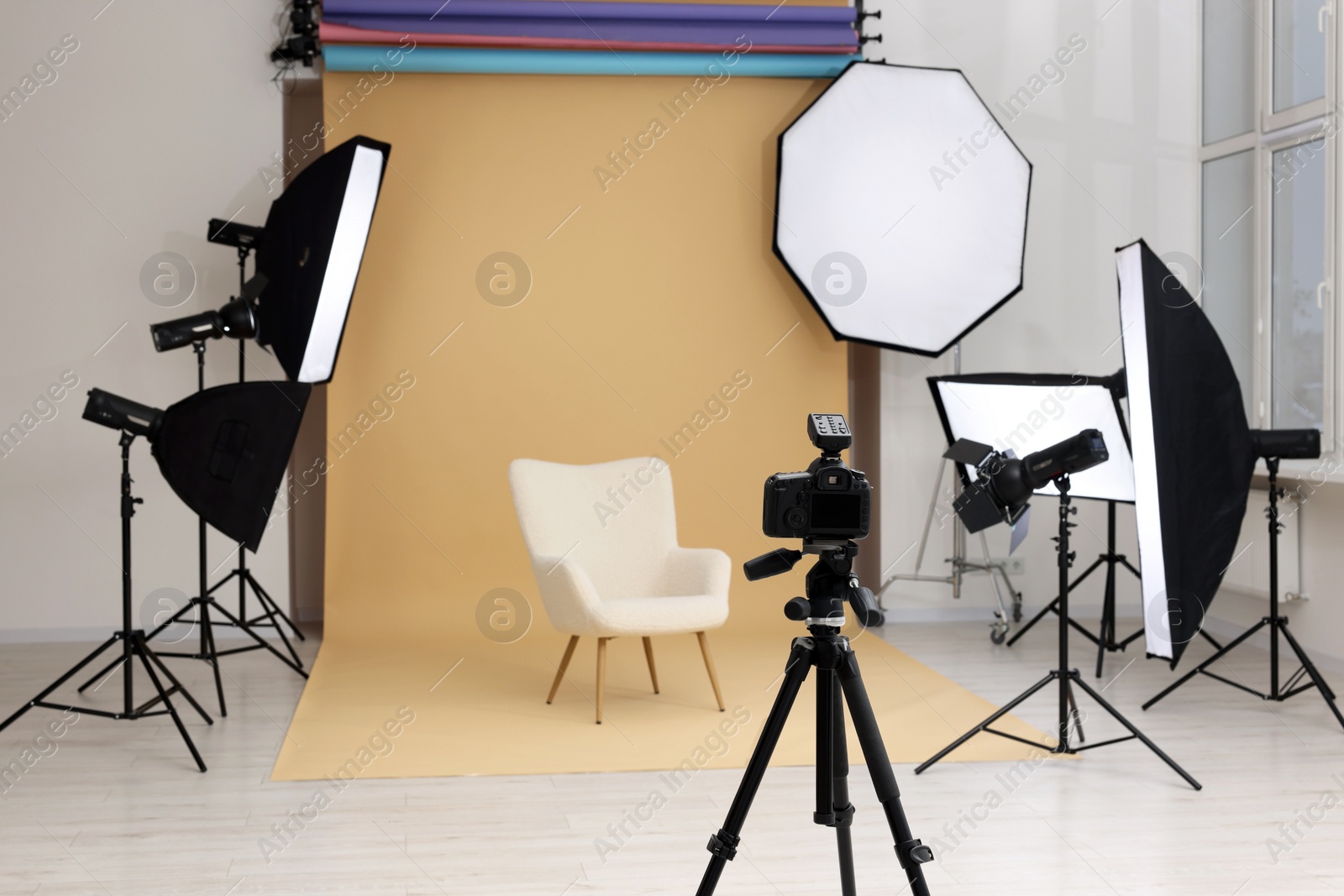 Photo of Camera on tripod, armchair and professional lighting equipment in modern photo studio, space for text