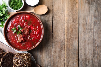 Photo of Stylish brown clay bowl with Ukrainian borsch on wooden table, flat lay. Space for text