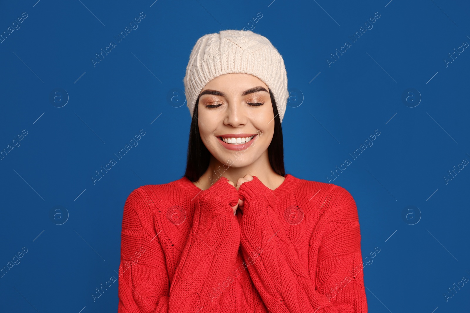 Photo of Young woman wearing warm sweater and hat on blue background. Winter season