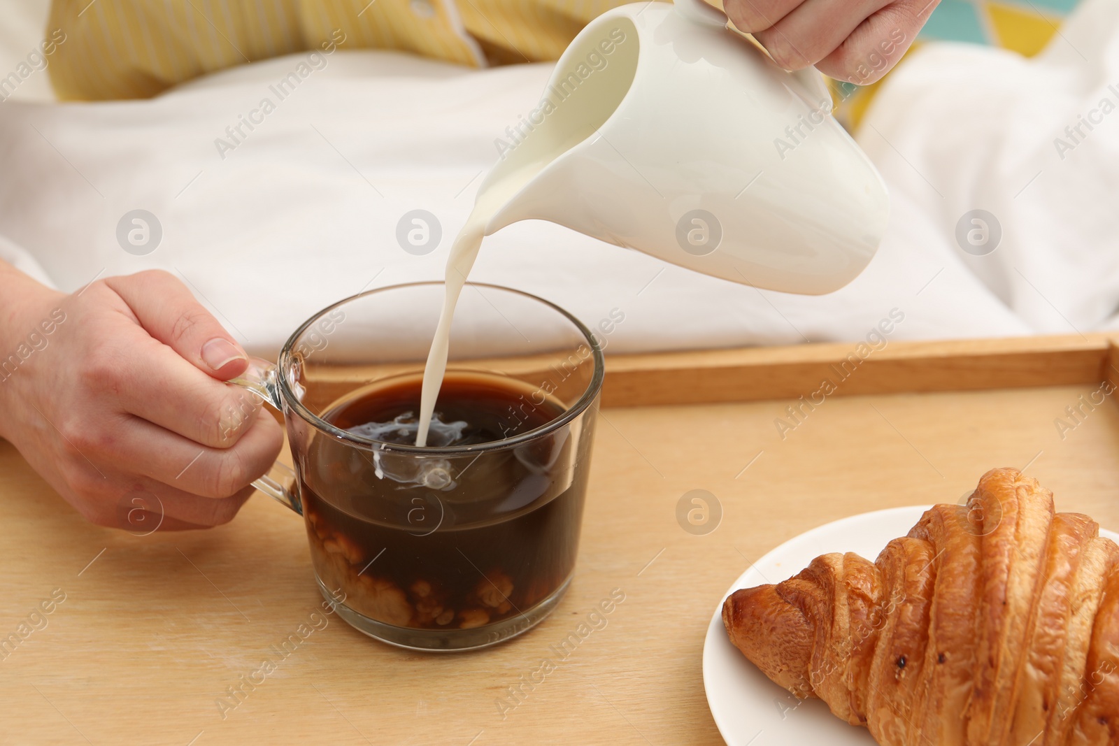 Photo of Woman pouring milk into cup with hot drink in bed, closeup