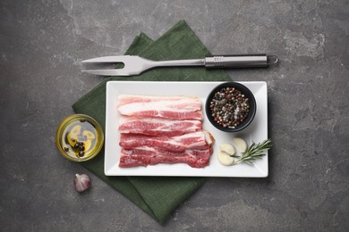 Photo of Pieces of raw pork belly, oil, peppercorns, rosemary and garlic on grey textured table, flat lay