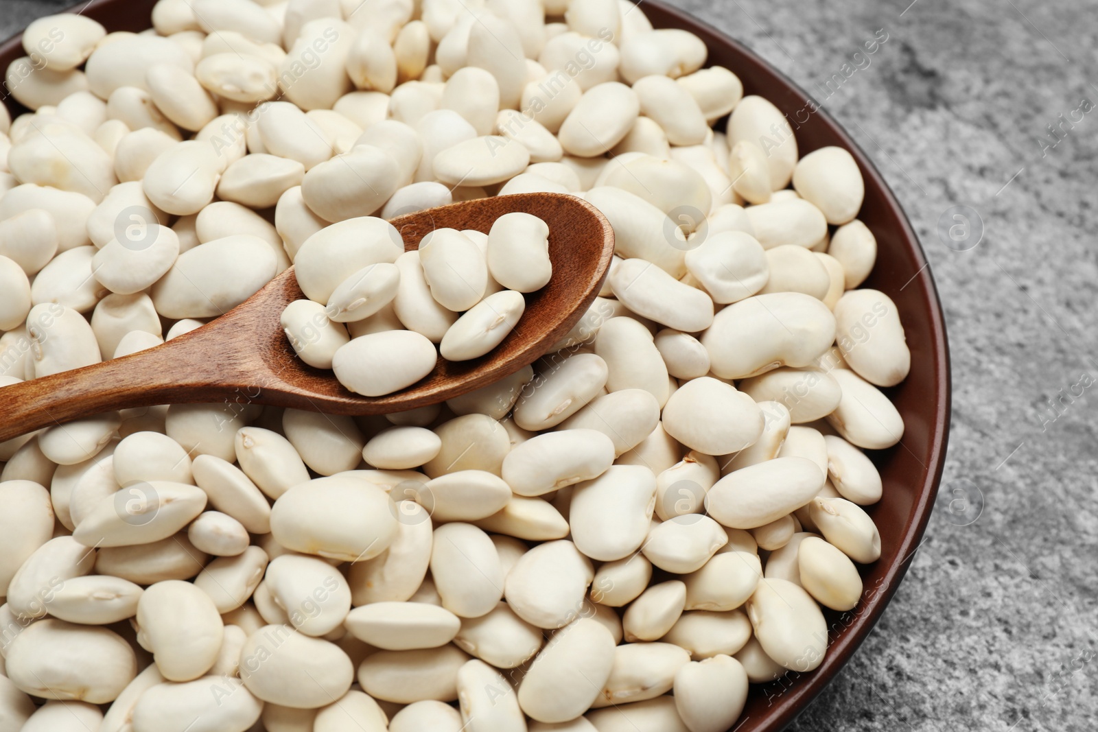 Photo of Raw white beans and spoon in bowl on grey table, top view