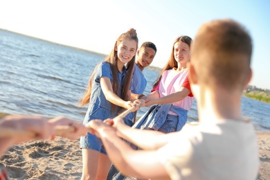 Photo of Group of children pulling rope during tug of war game on beach. Summer camp