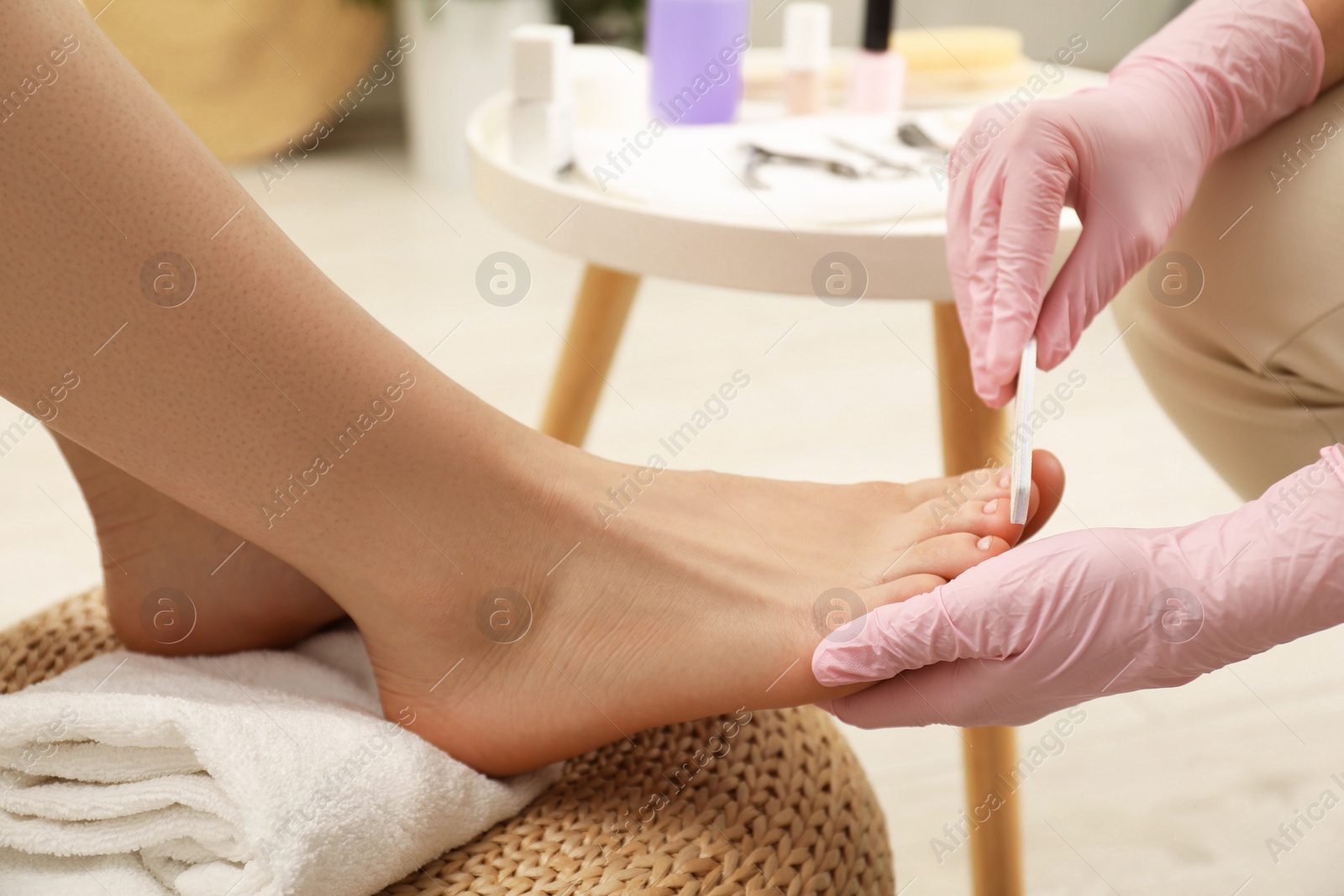 Photo of Professional pedicurist filing client`s toenails in beauty salon, closeup