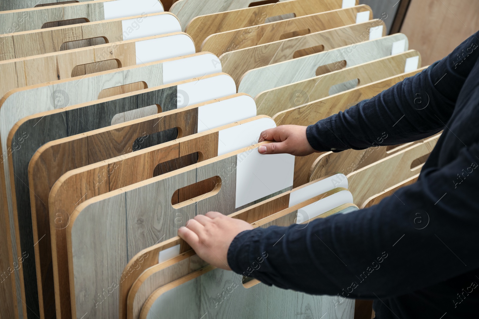 Photo of Man choosing wooden flooring among different samples in shop, closeup