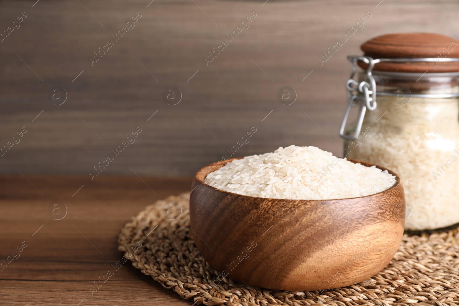 Photo of Bowl and jar with uncooked rice on wooden table