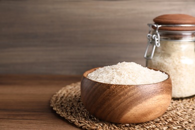 Photo of Bowl and jar with uncooked rice on wooden table