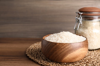 Bowl and jar with uncooked rice on wooden table