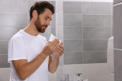 Photo of Handsome man with tube of cream in bathroom