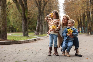 Photo of Portrait of happy mother and her children with autumn leaves in park, space for text