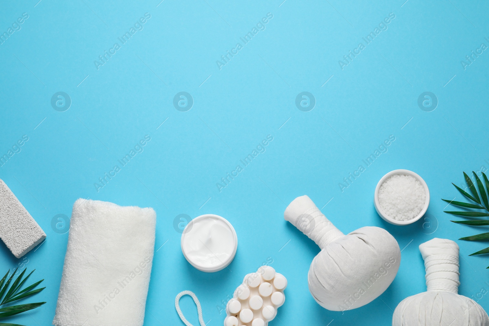 Photo of Beautiful spa composition with herbal massage bags and different care products on light blue background, flat lay. Space for text