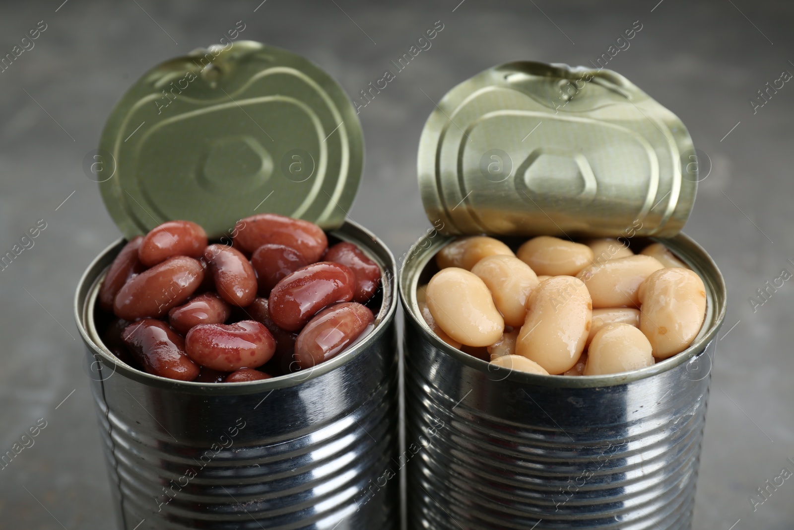 Photo of Tin cans with different canned kidney beans on grey table, closeup