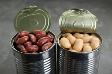 Photo of Tin cans with different canned kidney beans on grey table, closeup