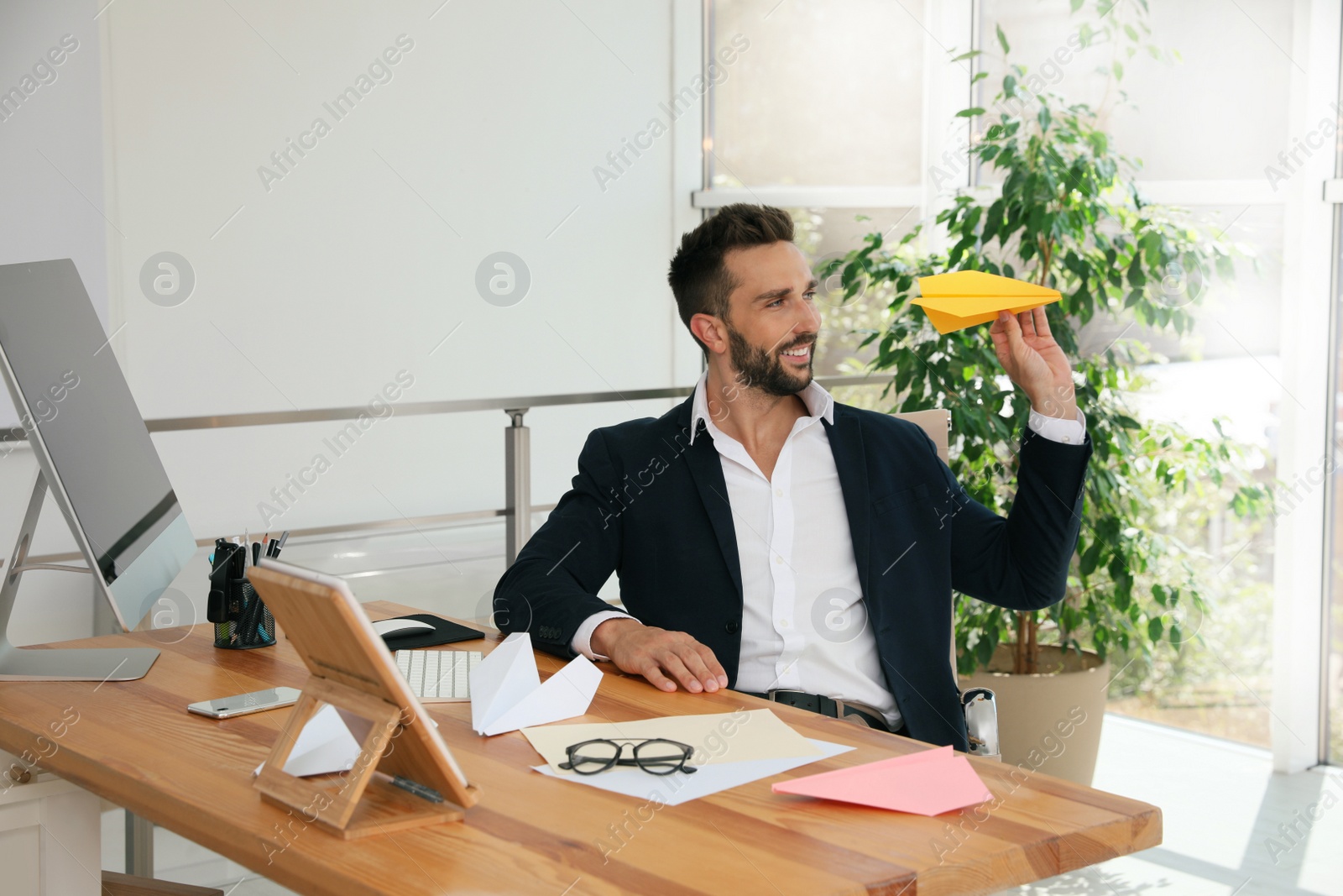 Photo of Handsome businessman playing with paper plane at desk in office