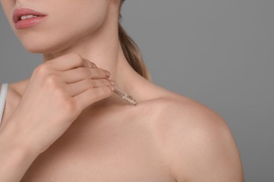 Photo of Woman applying essential oil onto collarbone on grey background, closeup. Space for text
