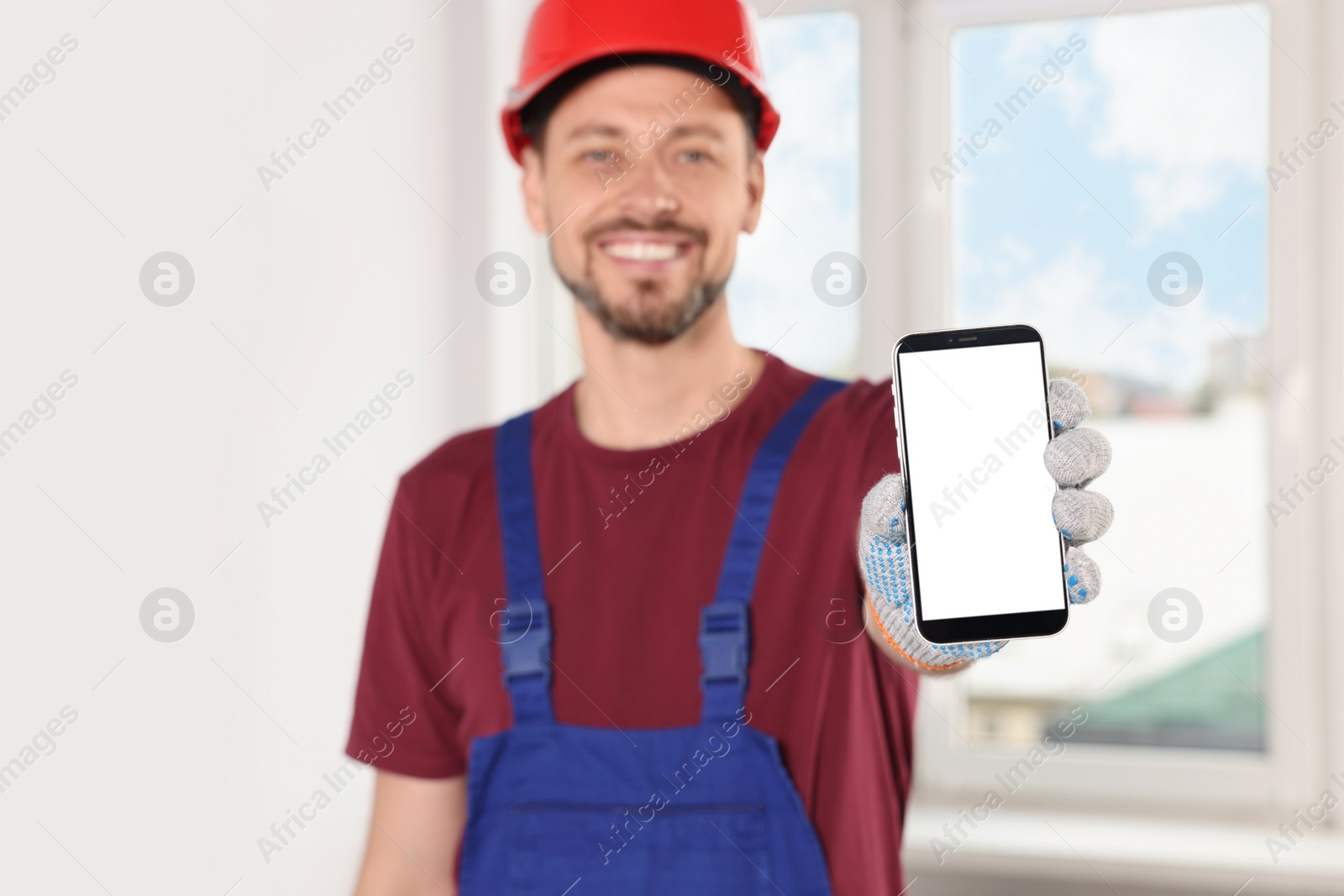 Photo of Professional repairman in uniform with phone indoors, focus on hand