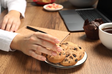 Photo of Bad habits. Woman eating cookies at wooden table, closeup