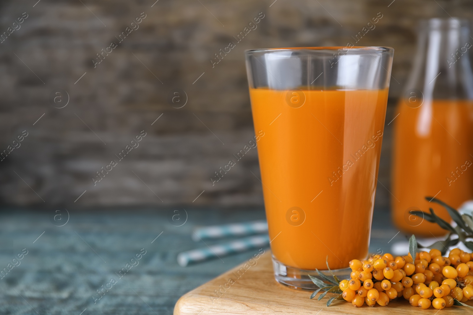 Photo of Delicious sea buckthorn juice and fresh berries on light blue table, closeup. Space for text