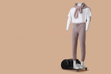 Photo of Male mannequin with sneakers and bag dressed in white t-shirt, sweater and pants on beige background, space for text