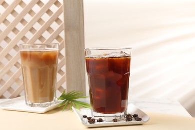 Photo of Refreshing iced coffee with milk in glasses and beans on beige table