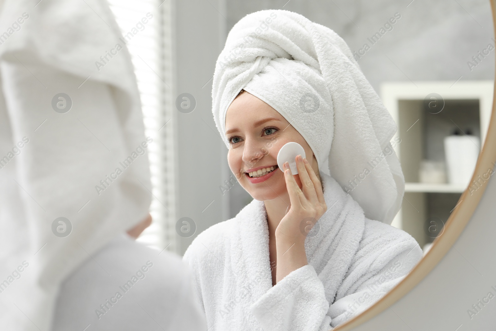 Photo of Smiling woman with freckles wiping face near mirror in bathroom