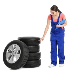 Female mechanic in uniform with car tires and clipboard on white background