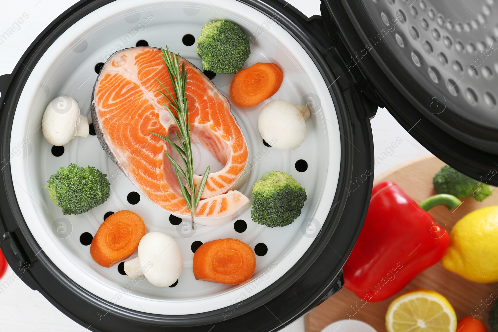 Photo of Salmon steak with garnish in multi cooker on table, top view