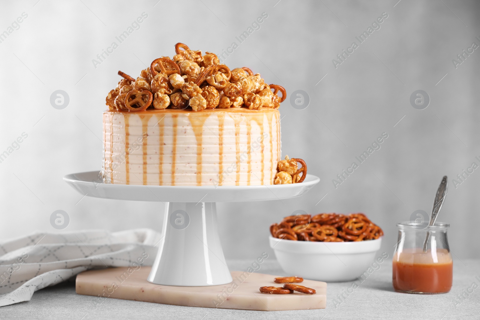 Photo of Caramel drip cake decorated with popcorn and pretzels on light table