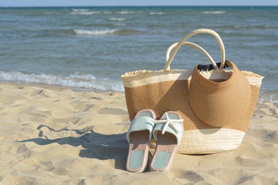 Stylish bag with slippers, visor cap and dry starfish on sandy beach near sea, space for text