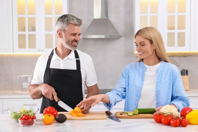 Photo of Happy affectionate couple cooking together at white table in kitchen