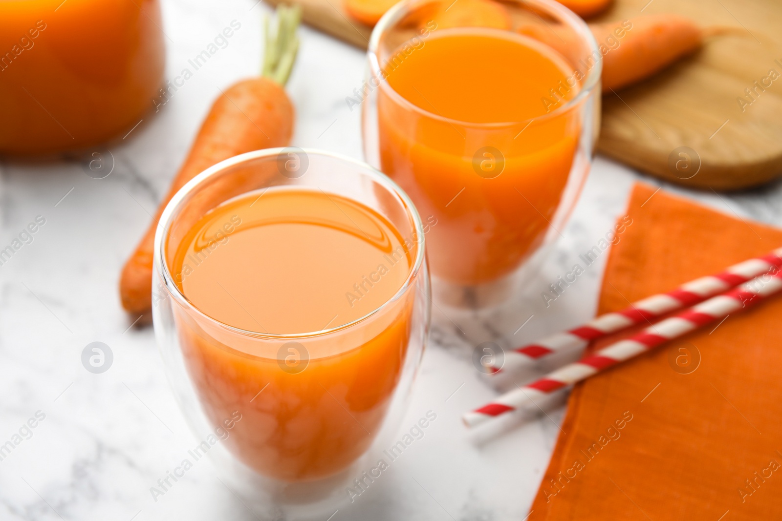 Photo of Freshly made carrot juice on white marble table, closeup