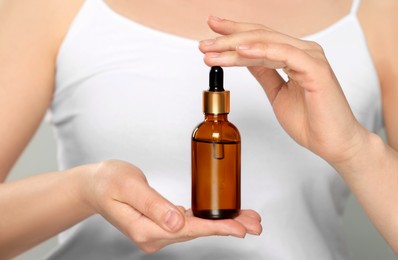 Woman holding bottle of essential oil on white background, closeup