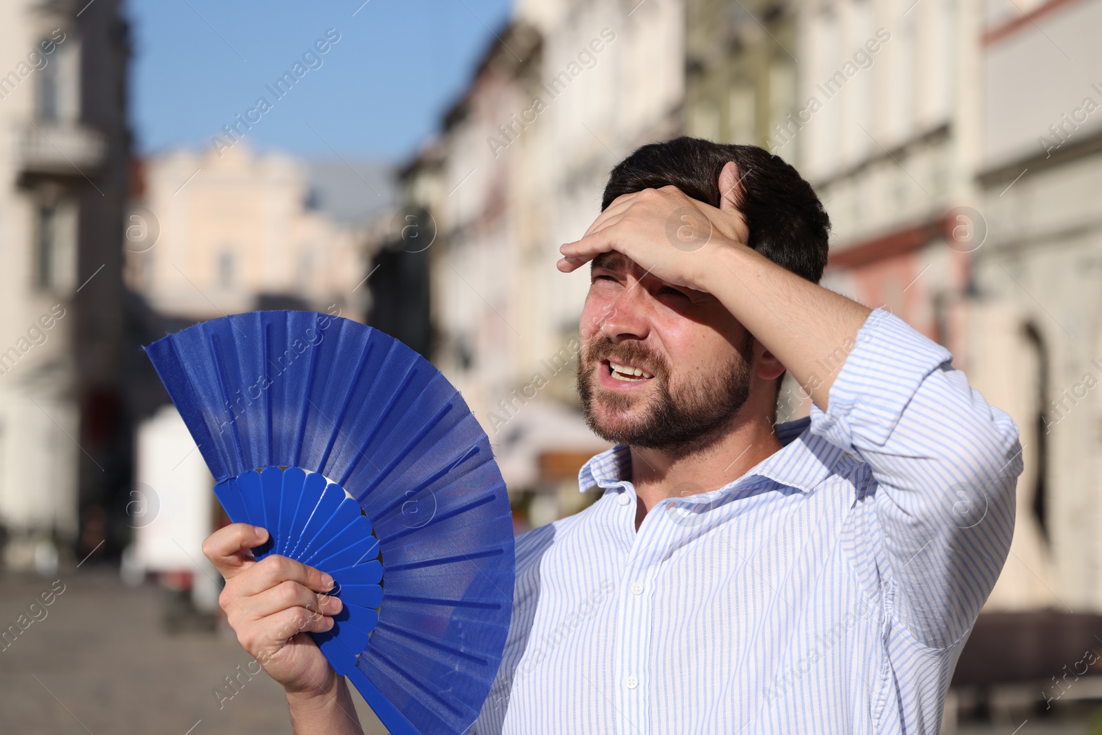 Photo of Man with hand fan suffering from heat outdoors