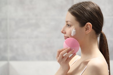 Photo of Young woman washing face with brush and cleansing foam indoors. Space for text