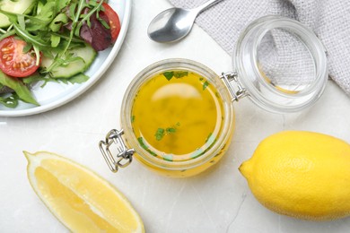 Jar with lemon dressing near salad on light table, flat lay