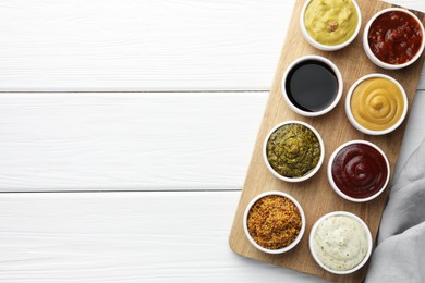 Many different sauces in bowls on white wooden table, top view. Space for text