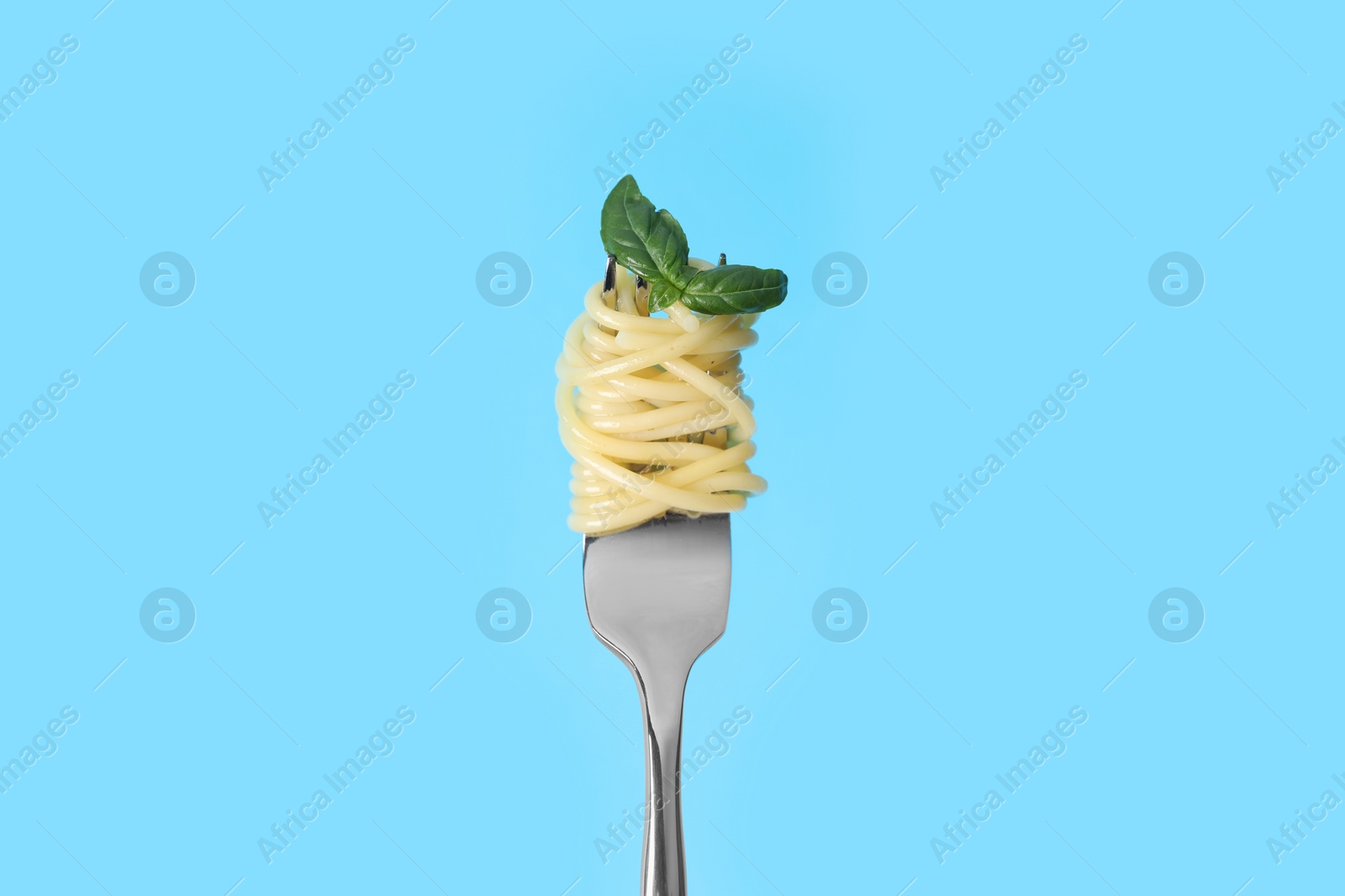 Photo of Fork with tasty pasta and basil on light blue background